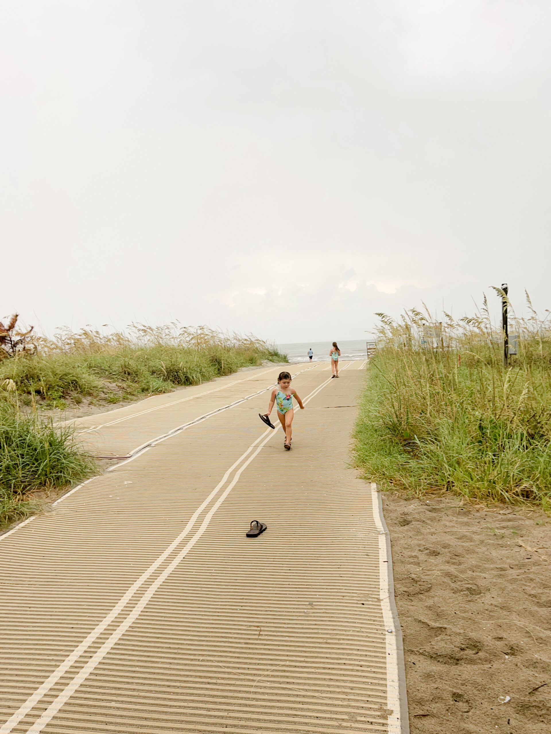 Child running on mat leading to beach.